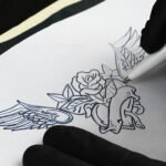 Artista del tatuaje que utiliza una impresora térmica y dibuja a mano sobre papel de transferencia para obtener plantillas transparentes.