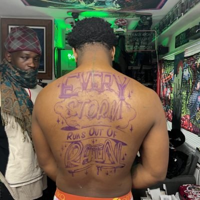 Customer’s "Every Storm Runs Out of Rain" art script tattoo work on back – fresh purple design of the client’s personalized tattoo in a studio setting