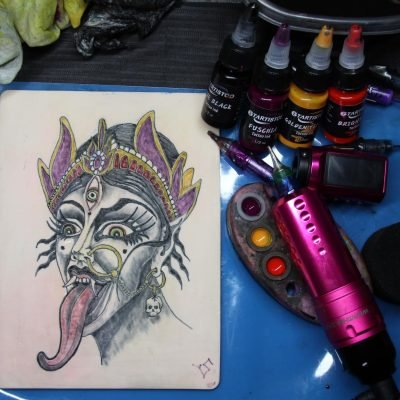 Tattoo artist setup: Gtartistoo Tattoo Ink bottles, intricate tattoo design on practice skin, tattoo machine, and ink palette with Gtartistoo ink shades